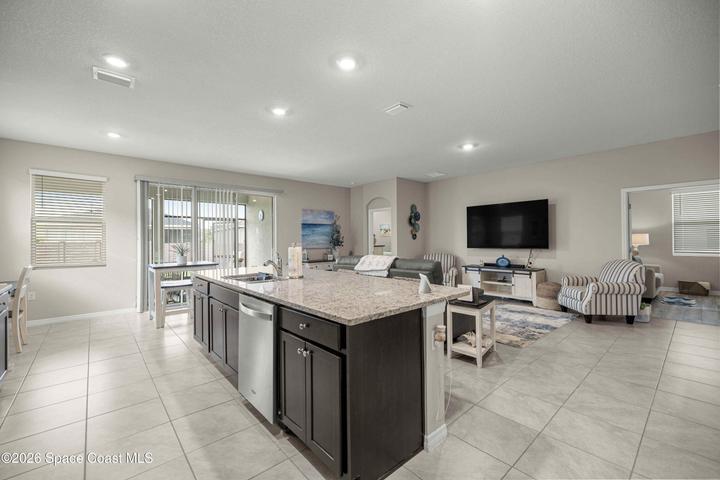 Spacious open-concept living area featuring a large kitchen island with a granite countertop, dark wood cabinetry, and an undermount stainless steel sink
