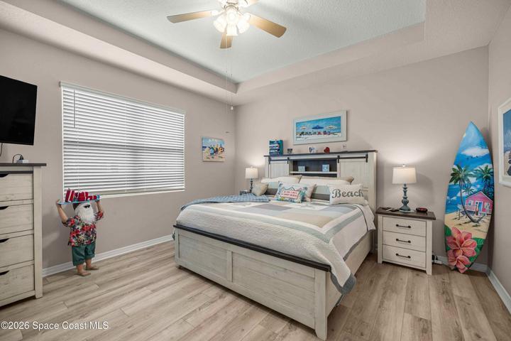 Bedroom featuring light wood-finish flooring, a tray ceiling, and a ceiling fan with integrated lighting