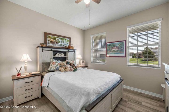 Bedroom featuring wood-finish flooring, two windows with blinds, and a ceiling fan with light fixture