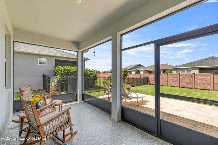 Spacious screened lanai featuring a grey speckled floor, direct access to the backyard, and a paver patio