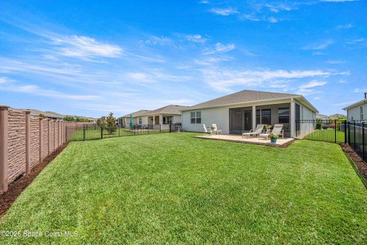Expansive backyard featuring a large concrete patio, screened lanai, lush lawn, and partial decorative privacy fencing