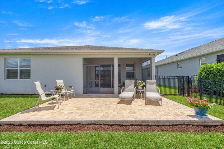 Expansive paver patio with a screened lanai, manicured lawn, and a black aluminum fence