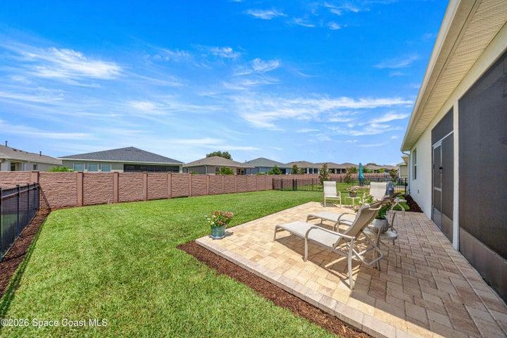 Expansive backyard featuring a paver patio with decorative border, manicured lawn, and a privacy fence
