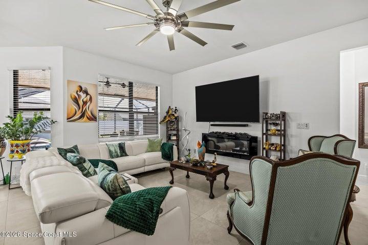 The spacious great room offers a comfortable gathering space, highlighted by a modern electric fireplace, oversized ceiling fan, and seamless connection to the kitchen, dining area, and outdoor living spaces.