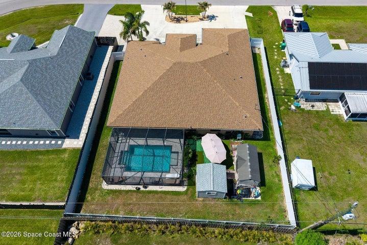 An elevated perspective showcases the screen-enclosed pool, covered lanai, fully fenced backyard, and two detached storage sheds, highlighting the thoughtful layout and generous outdoor living space.