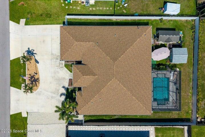 A bird's-eye view highlights the home's expansive footprint, circular driveway, screen-enclosed pool, fully fenced yard, and detached storage sheds, offering a unique perspective of the property's design and functionality.