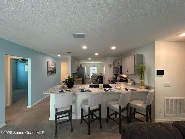 Open-concept kitchen featuring light-toned cabinetry with dark hardware, stainless steel appliances, a large peninsula seats 4, with a gooseneck faucet, and light-toned countertops.