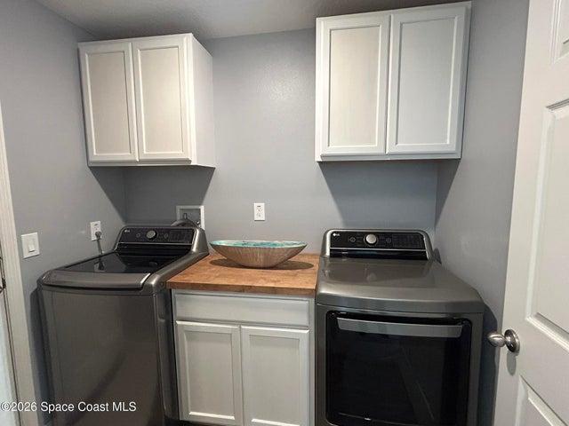 Laundry area featuring white shaker-style cabinetry, a wood-finish countertop, and neutral wall paint