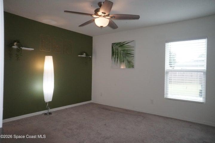 Primary bedroom featuring a dark green accent wall, white baseboards, and a ceiling fan with integrated lighting