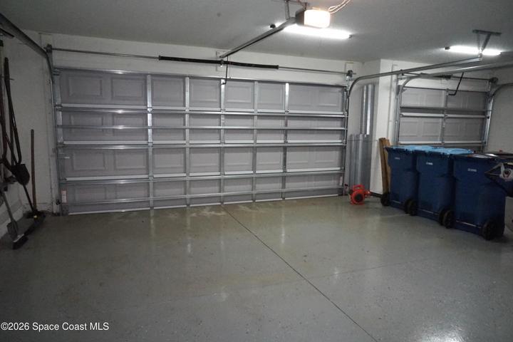 Spacious 3 car garage featuring two sectional doors, overhead lighting, and a durable epoxy-coated floor and pull-down stairs to attic access.