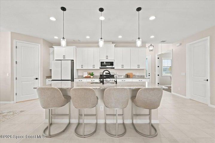 Gourmet kitchen with oversized island, seating for four, quartz counters, and pendant lighting, the heart of this Melbourne, FL home