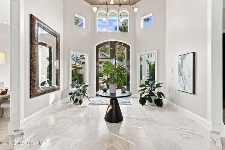 Grand two-story foyer featuring soaring ceilings, an abundance of natural light, elegant arched windows, beautiful travertine stone flooring, and dramatic mahogany double entry doors.