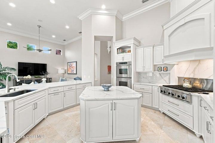 Beautifully appointed chef’s kitchen featuring custom cabinetry, expansive quartz countertops, an oversized center island, professional-style gas range, double ovens, and an open design flowing seamlessly into the adjoining living space.
