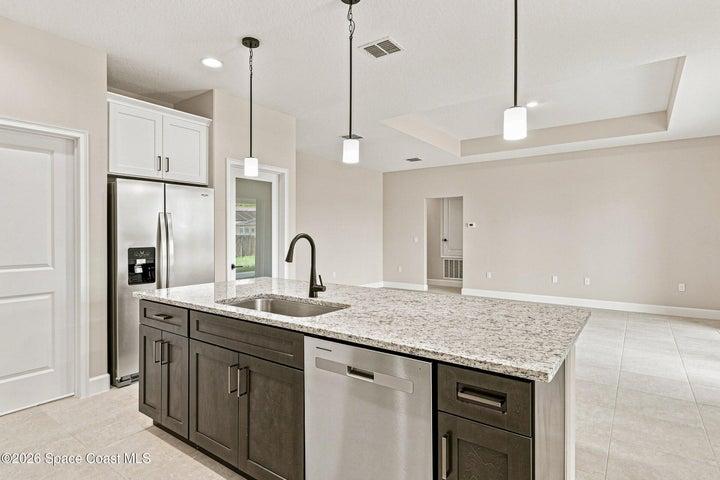 The Kitchen features granite countertops, two-tone solid wood soft-close cabinetry, stainless steel appliances, a walk-in pantry, and crown molding paired beautifully with black handles and fixtures.