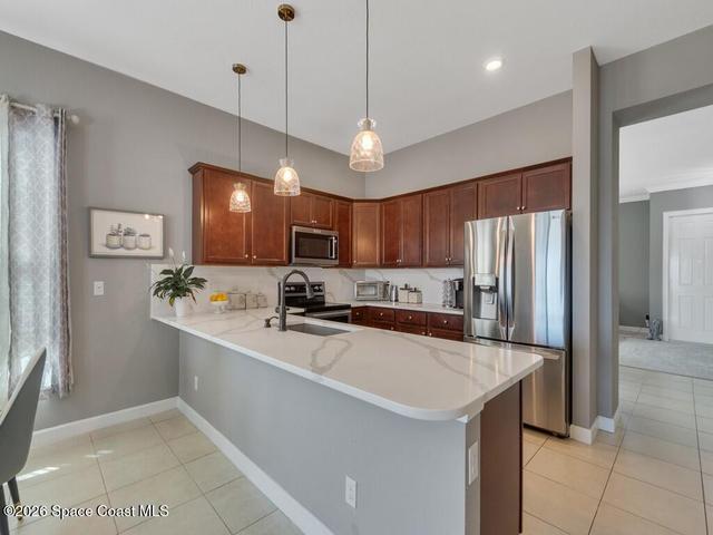 Modern kitchen featuring dark wood cabinetry, stainless steel appliances, a white stone-finish countertop, a tile backsplash, and recessed lighting