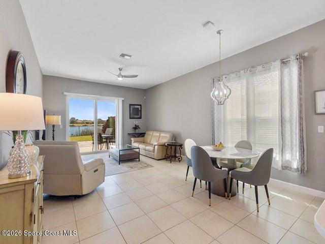 Open-concept living area featuring light-toned tile flooring, a contemporary ceiling fan, and a decorative pendant light fixture