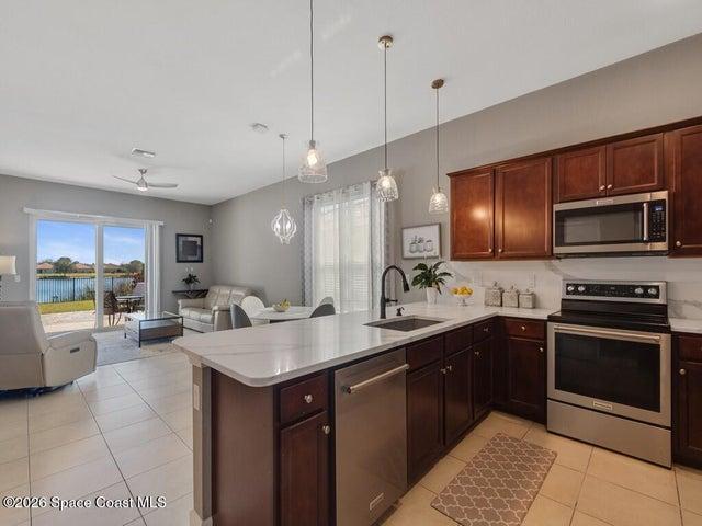 Open-concept kitchen featuring an island with white countertop, dark wood-finish cabinetry, and stainless steel appliances