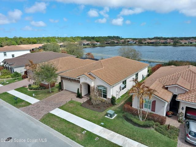 Mediterranean-style residence featuring a tile roof, paver driveway, manicured landscaping, and a waterfront location