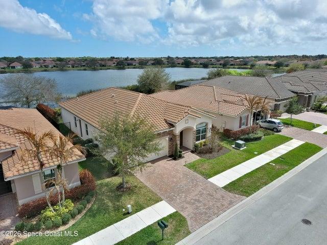 Mediterranean-style residence featuring a tile roof, paver driveway, manicured landscaping, and a waterfront location