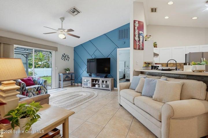 Vaulted ceiling, ceiling fan, tile flooring, sliding glass door access to outdoor space, and a kitchen pass-through with a breakfast bar
