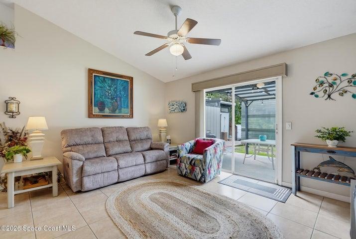 Vaulted ceiling with a ceiling fan, tiled flooring, and sliding glass doors leading to a covered patio