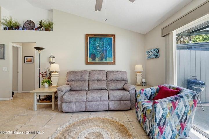 Cathedral ceiling with a decorative ledge, sliding glass door, tile flooring, and light wall finishes