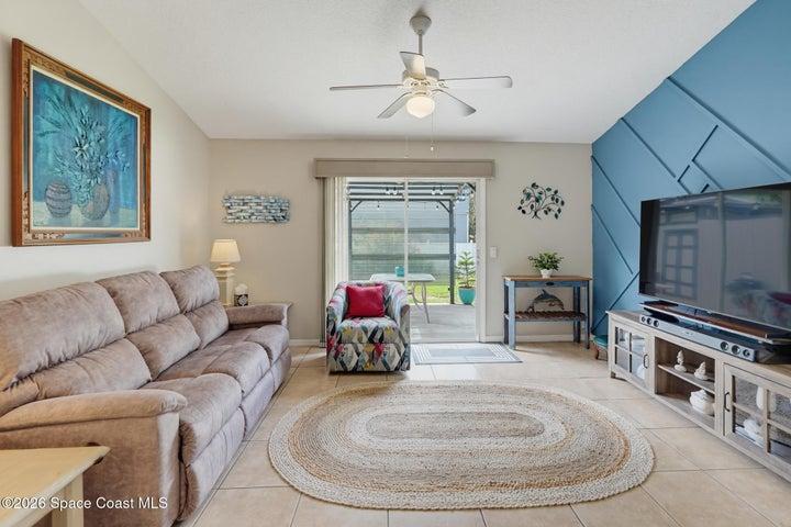 Tiled flooring throughout, ceiling fan with integrated lighting, built-in entertainment console, sliding glass doors, and a decorative accent wall