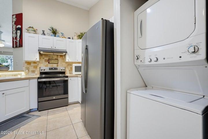 White cabinetry, tile flooring, stainless steel range, stacked washer and dryer, and a stainless steel refrigerator
