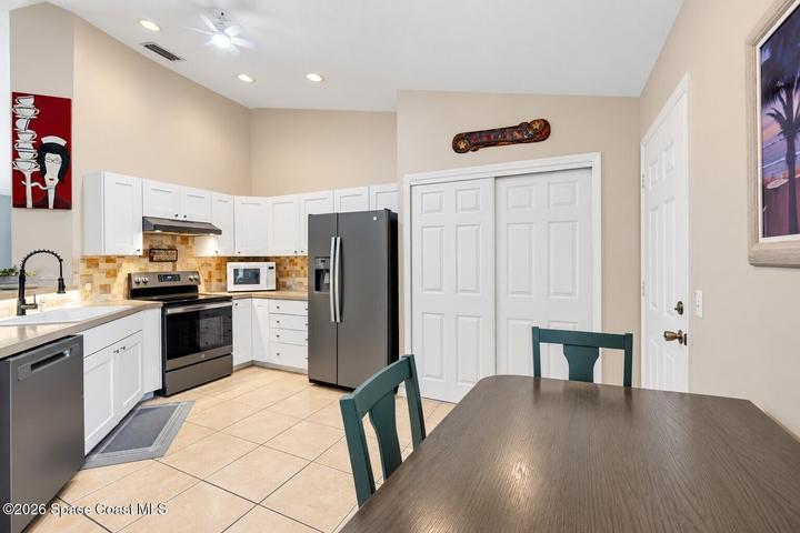 Kitchen featuring white cabinetry, stainless steel appliances, tile flooring, and a vaulted ceiling with recessed lighting