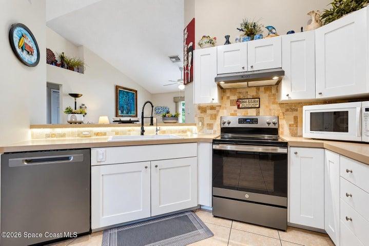 Kitchen featuring white shaker-style cabinetry, stainless steel appliances, a tile backsplash, and an undermount sink with a gooseneck faucet
