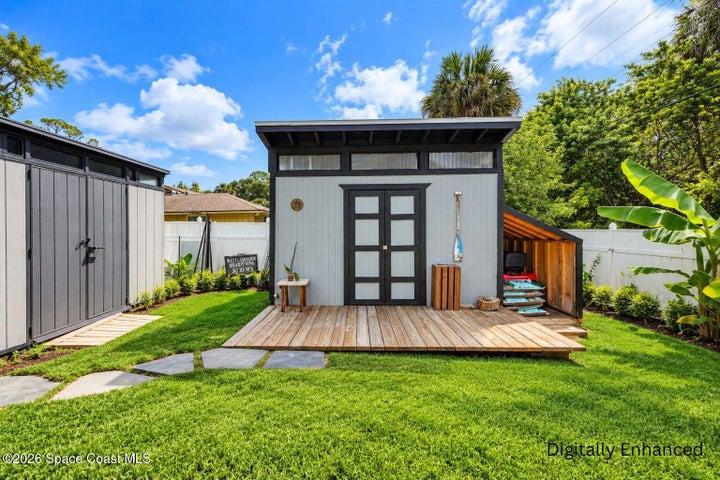 Manicured lawn with stepping stones, modern shed with transom windows, double doors, and an attached wood-clad storage area, accompanied by a spacious wood deck