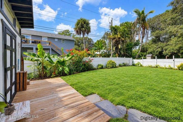 Expansive backyard featuring a manicured lawn, a white privacy fence, and mature tropical landscaping