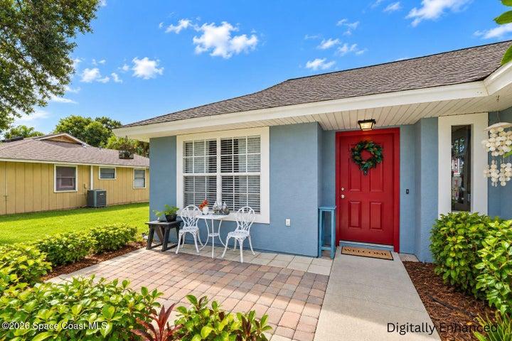 Front exterior featuring a red entry door, shingled roof, light blue siding, and a paver patio