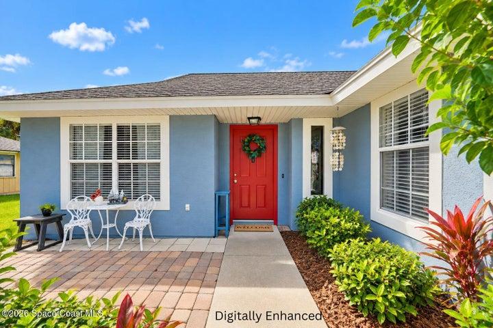 Front exterior featuring a red entry door, shingled roof, light blue siding, and a paver patio